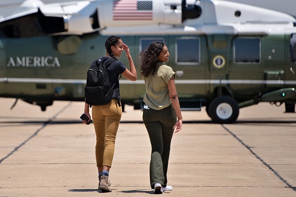 Malia Obama (L) and Sasha Obama walk to a helicopter while looking back at their parents at Roswell International Air Center June 17, 2016 in Roswell, New Mexico. / AFP / Brendan Smialowski (Photo credit should read BRENDAN SMIALOWSKI/AFP/Getty Images)